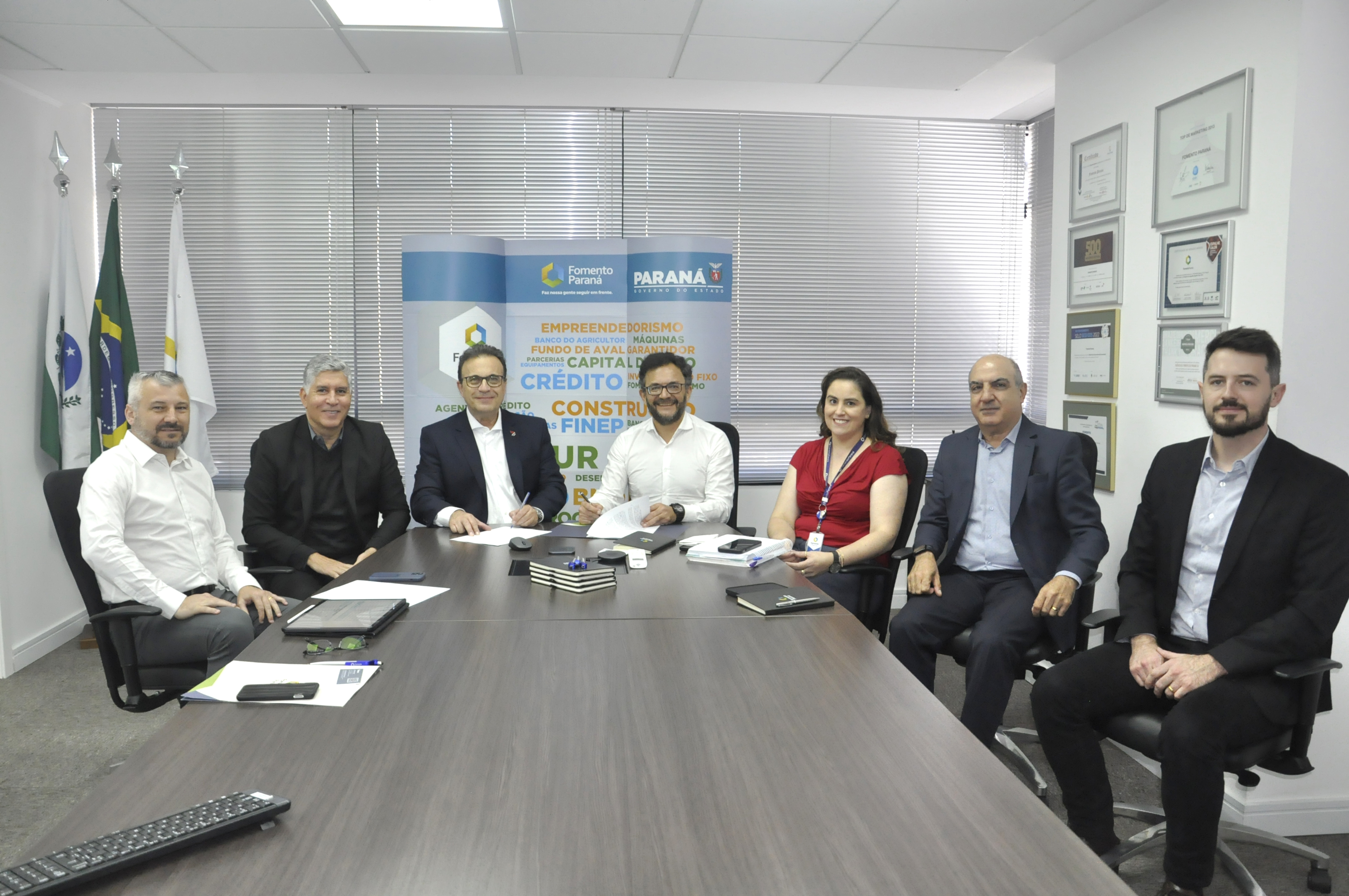Reunião entre diretores da Fomento paraná e do BDMG em uma sala com uma grande mesa de reuniões